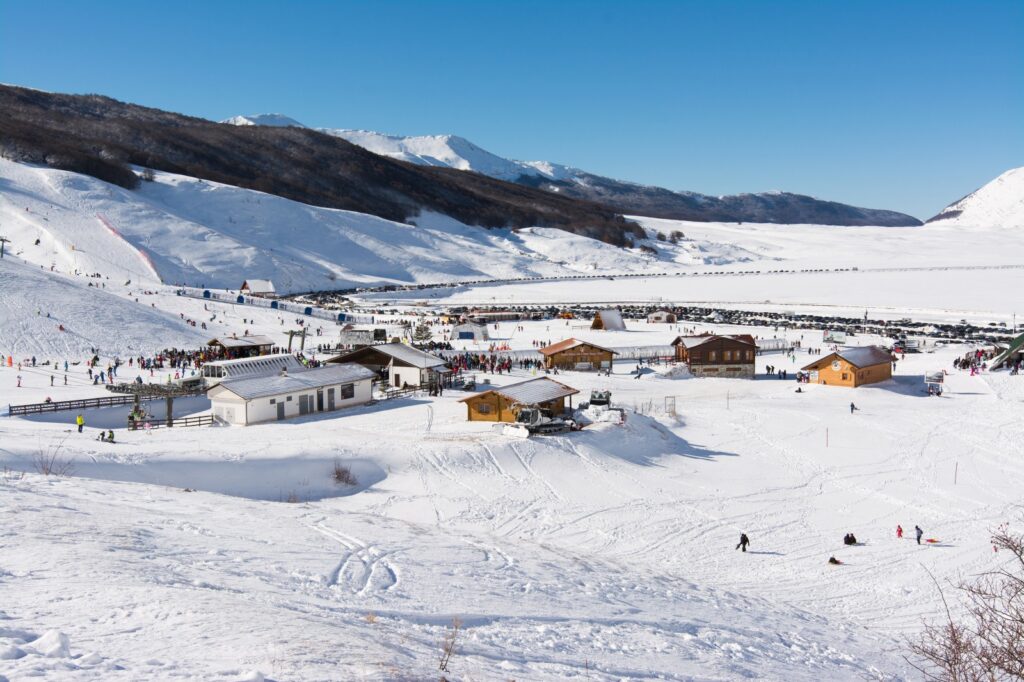 Panoramica della stazione sciistica di Campo Felice, con piste innevate, rifugi e visitatori che praticano sport invernali su un altopiano circondato dalle montagne abruzzesi.